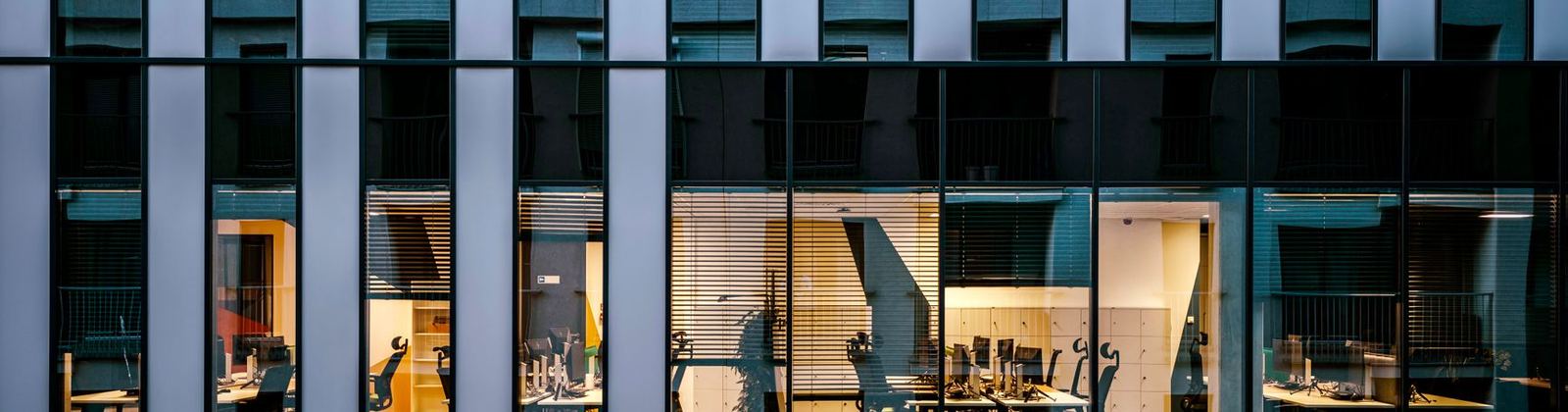 Lit office floors seen through the glass facade of a building at dusk